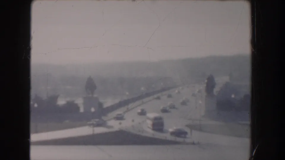 1960 Washington DC home-movie frame showing light traffic on a bridge or elevated roadway, with water, trees, and haze in the distance.