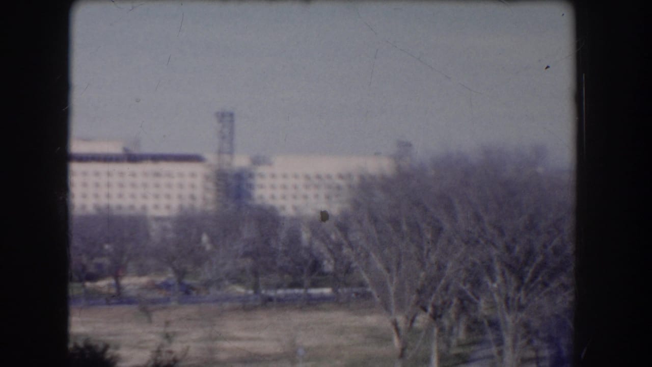 Distant building partly screened by bare trees, with open ground in the foreground.