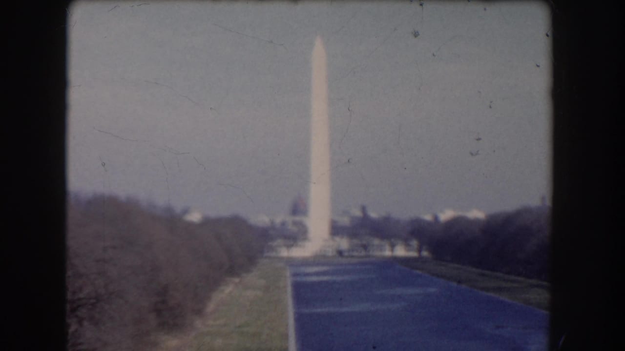 Distant Washington Monument viewed from a tree-lined walkway with dark film borders.