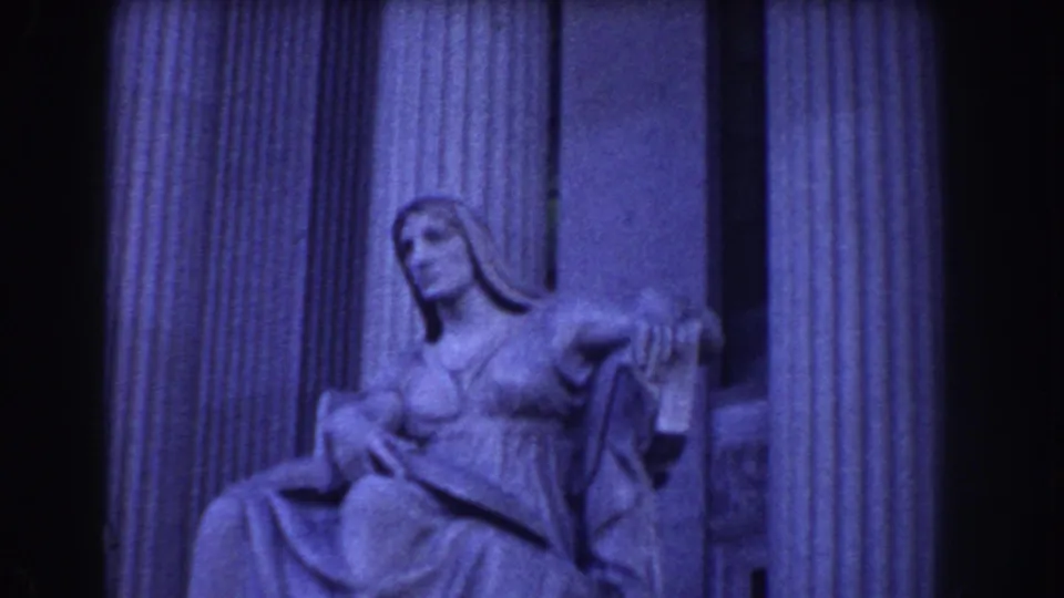 Blue-tinted 8mm frame of a classical seated statue inside or near a columned structure in Washington, DC.