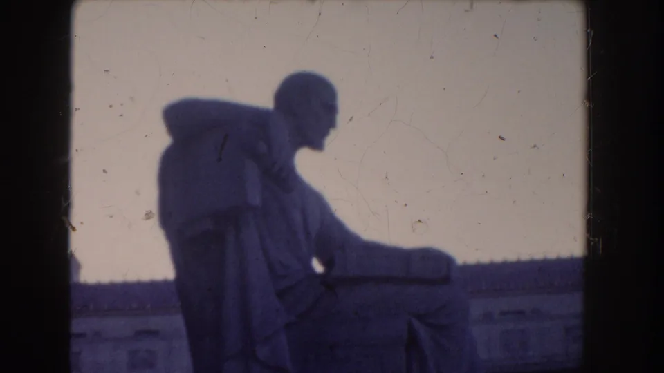 1960 Washington DC home-movie frame showing the statue in side profile, with a pale sky, roofline, and visible film wear.