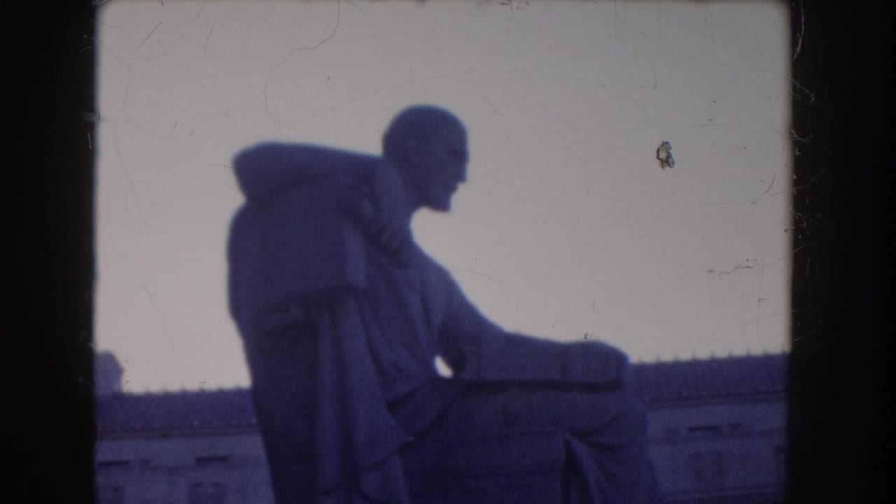 1960 Washington DC home-movie frame showing a seated statue near the National Archives, filmed in soft blue-tinted 8mm light.