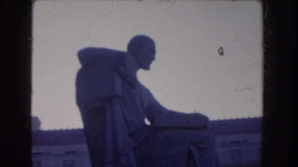 1960 Washington DC home-movie frame showing a seated statue near the National Archives, filmed in soft blue-tinted 8mm light.