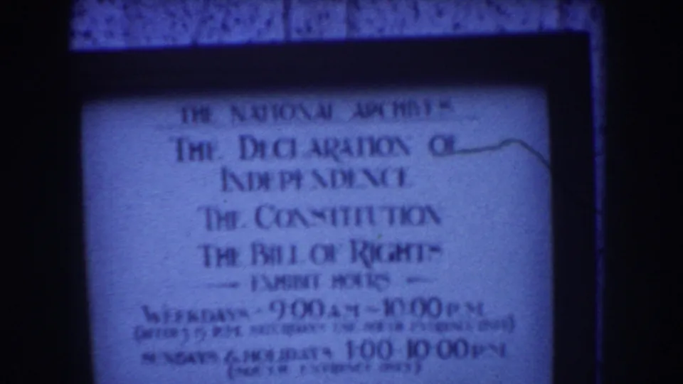 Blue-tinted 8mm frame showing the National Archives sign with founding-document titles and visitor hours partly legible.