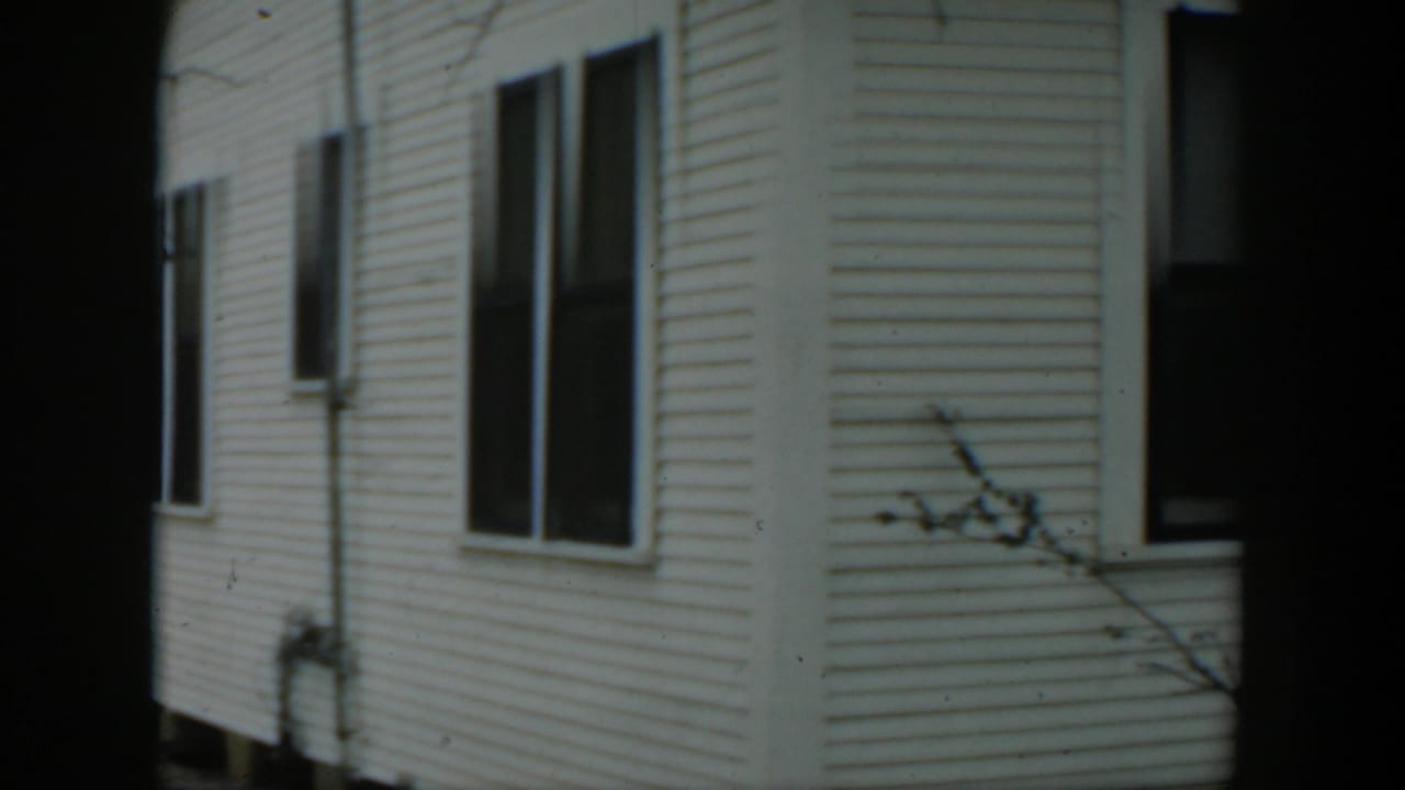 Side of a white clapboard house with dark windows and a dark vertical film border.