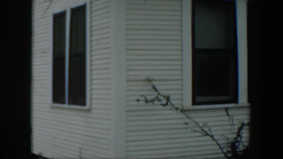 1951 Cuba home-movie view of a clapboard house facade with two dark windows and bare branches crossing the lower frame.