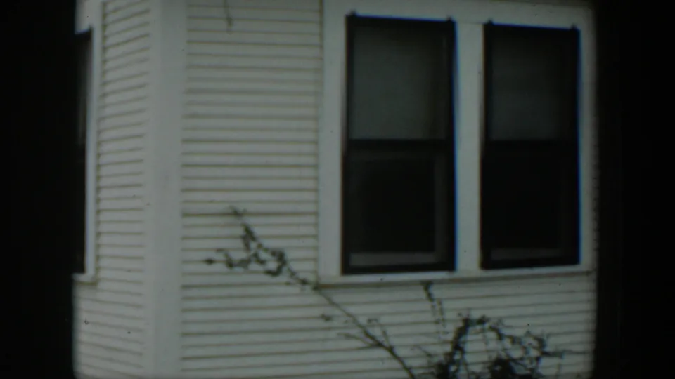 1951 Cuba 8mm frame showing a white clapboard house facade with paired dark windows, bare branches, and soft film grain.