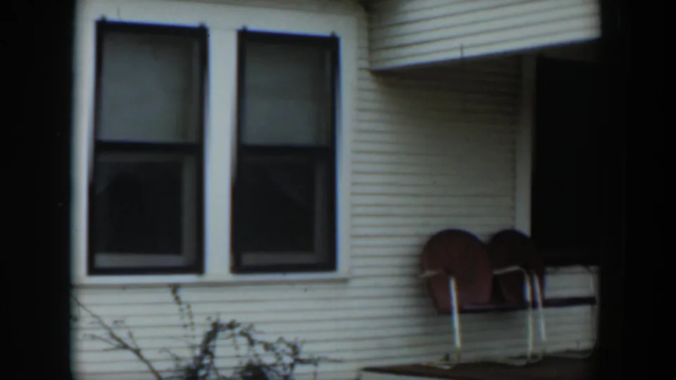 1951 Cuba frame with two brown curved-back porch chairs near dark windows on a white clapboard house.