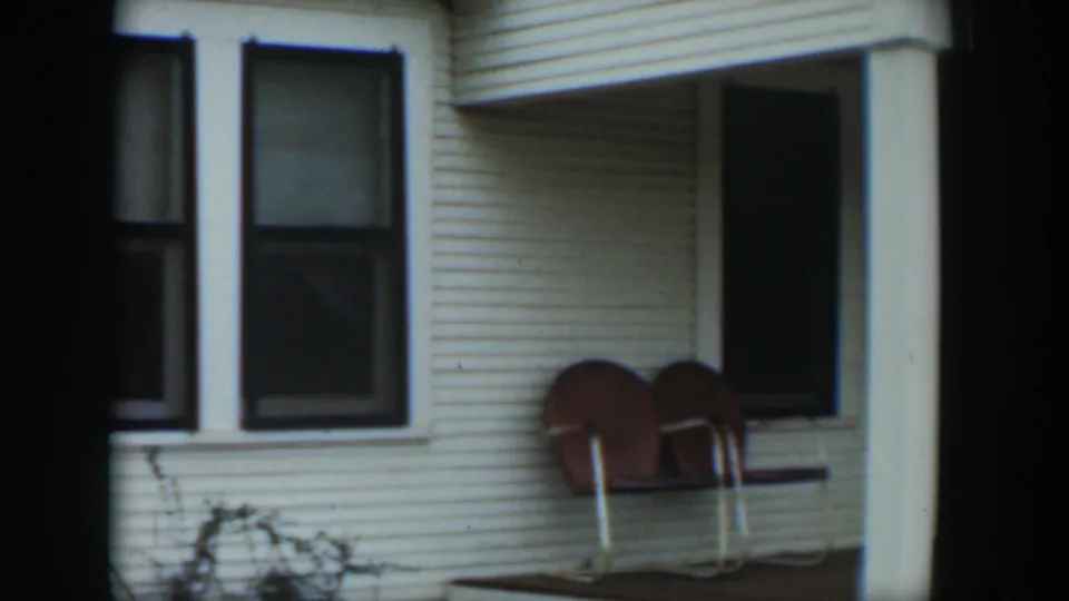 1951 Cuba home-movie frame showing the porch corner, two brown chairs, a square post, and dark window openings.