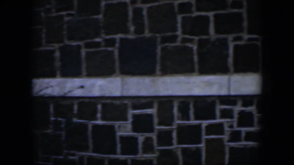 The frame shows a shaded stone block exterior in Cuba, with a pale horizontal band and foreground darkness from trees or structure.