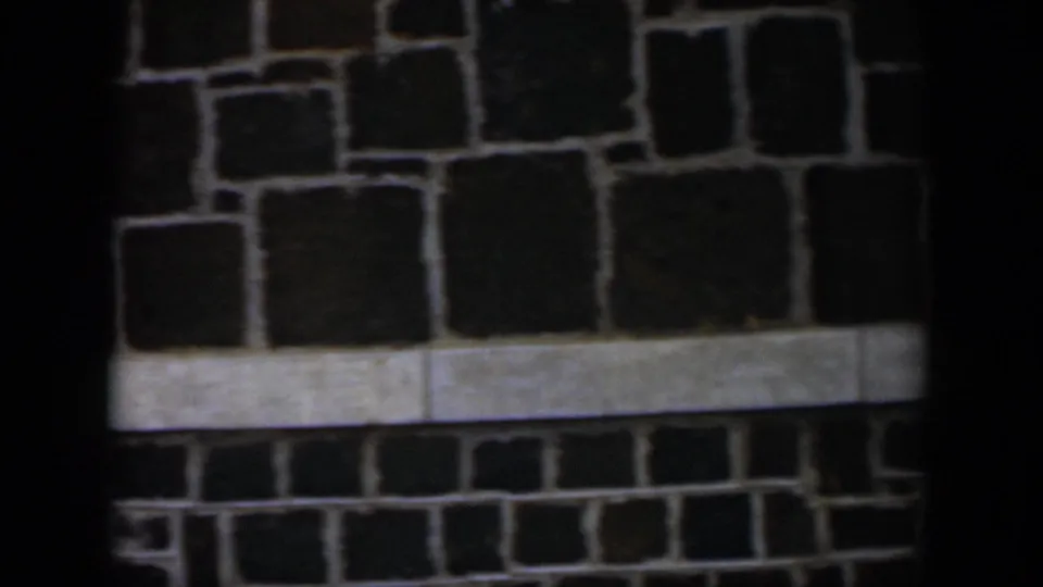 1951 Cuba 8mm frame showing a dark irregular stone wall crossed by a pale horizontal ledge or trim band.