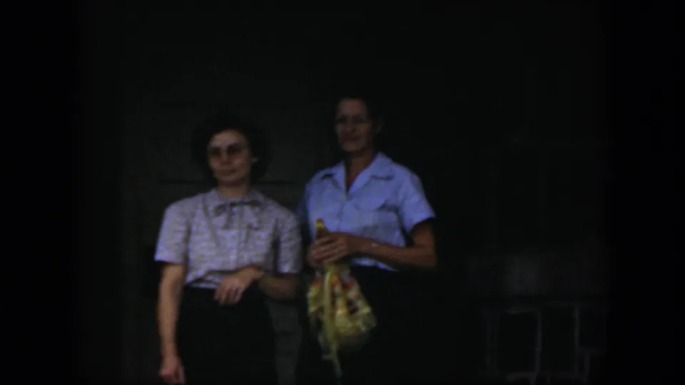 In the clearest frame, two adult women in 1951 Cuba stand by a doorway, smiling faintly as one holds a patterned bag.