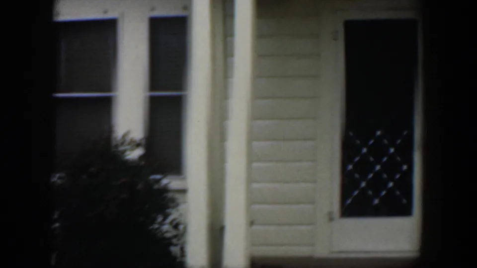1951 Cuba home-movie view of the same house front, with paired windows, a porch column, shrubs, and a dark doorway or door panel at the right.
