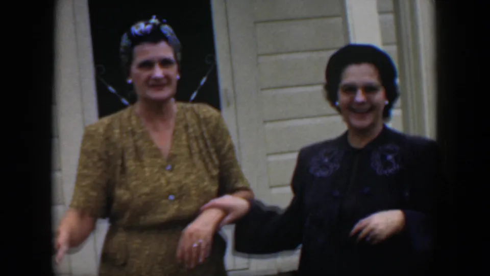 1951 Cuba home-movie frame with two adult women in mid-century clothing smiling near the doorway of a light clapboard house.