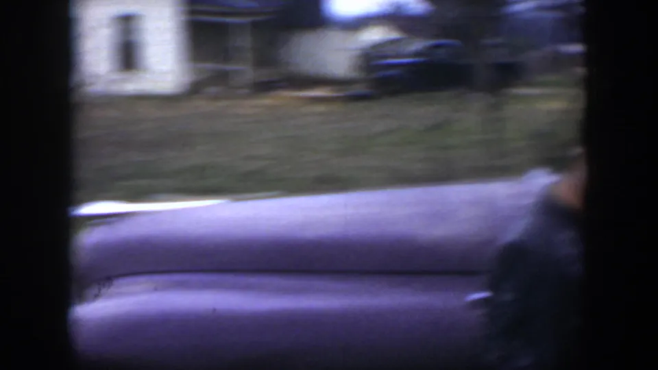 A vintage purple car fills the lower frame while the background yard, trees, and light house blur with handheld 8mm motion.