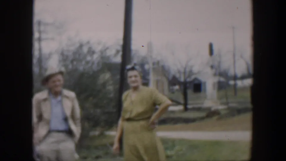 1951 Cuba frame of a man in light clothing and a woman in a green dress standing outdoors near utility poles and grass.
