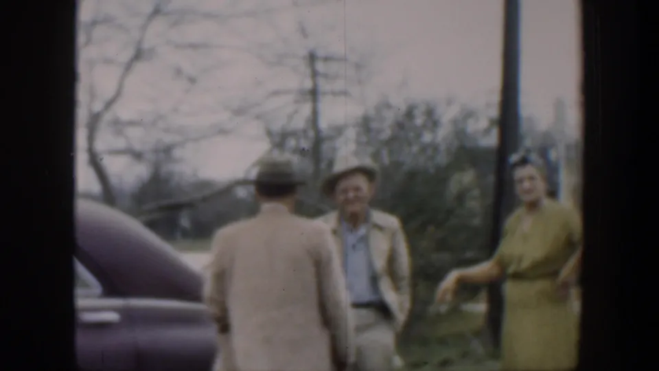 A second man with his back to the camera appears near a dark car while the woman in yellow and the man in a hat remain in the outdoor Cuba scene.