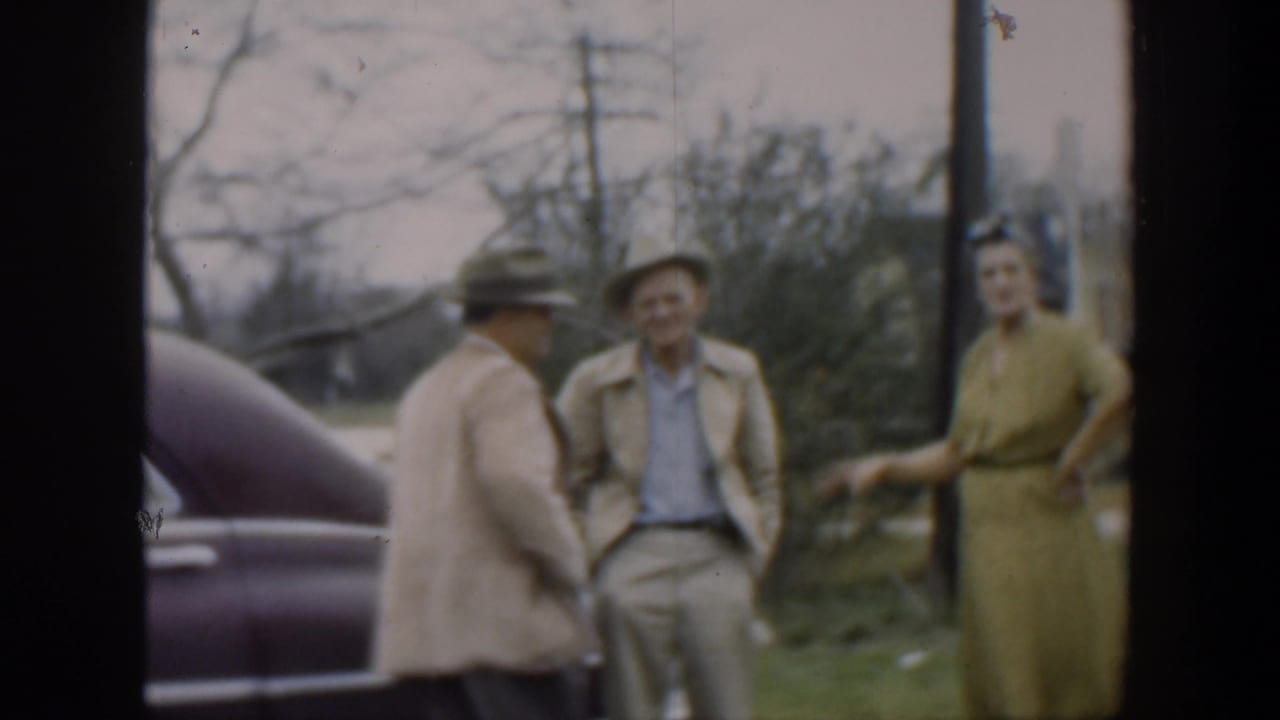 In 1951 Cuba home-movie footage, two men in hats and a woman in a green dress stand beside a purple vintage car outdoors.