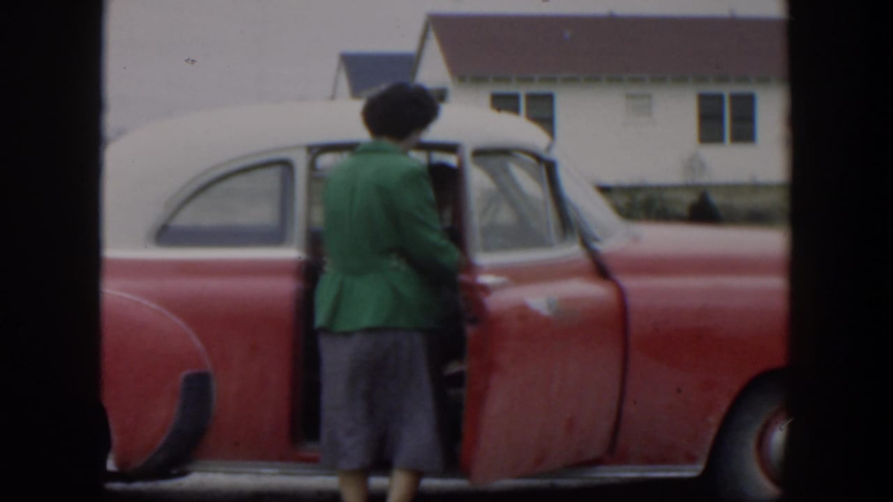 Woman in a green jacket stands beside an open red-and-white car door.