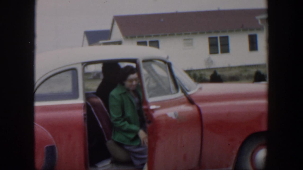 Woman sits partly inside the open red-and-white car as the door remains open.