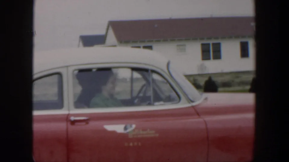 The woman remains in the driver's seat of the red-and-white car, seen through the side window in 1951 Cuba home-movie footage.