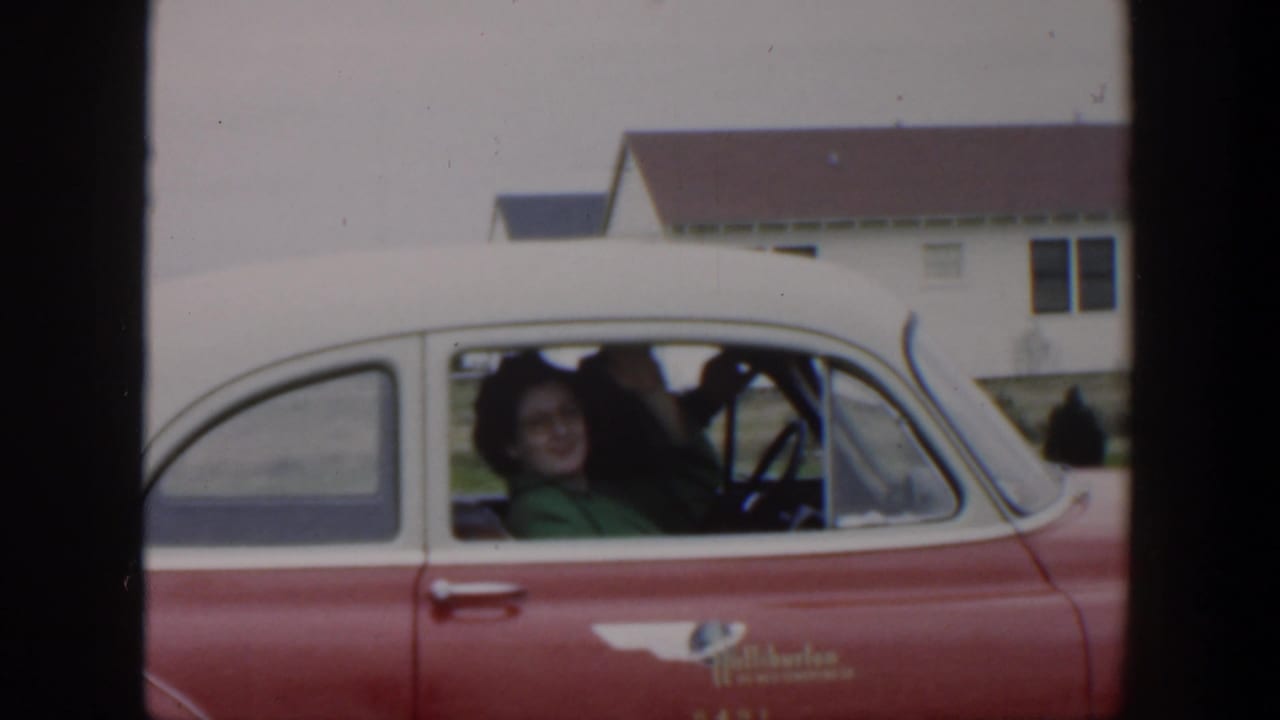 Woman in a green top smiles from the passenger seat of a red and white car.