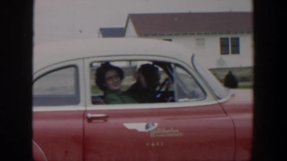 1951 Cuba 8mm frame showing a woman passenger facing the camera while the driver sits beside her in the red and white car.