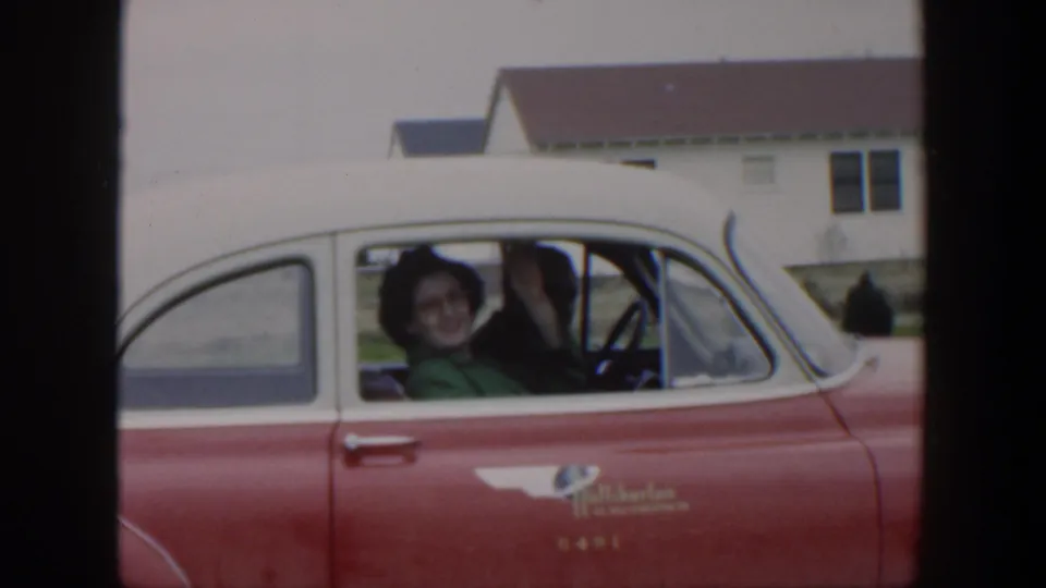 1951 Cuba home-movie frame with a woman smiling and waving from the passenger window of a red and white 1950s car.
