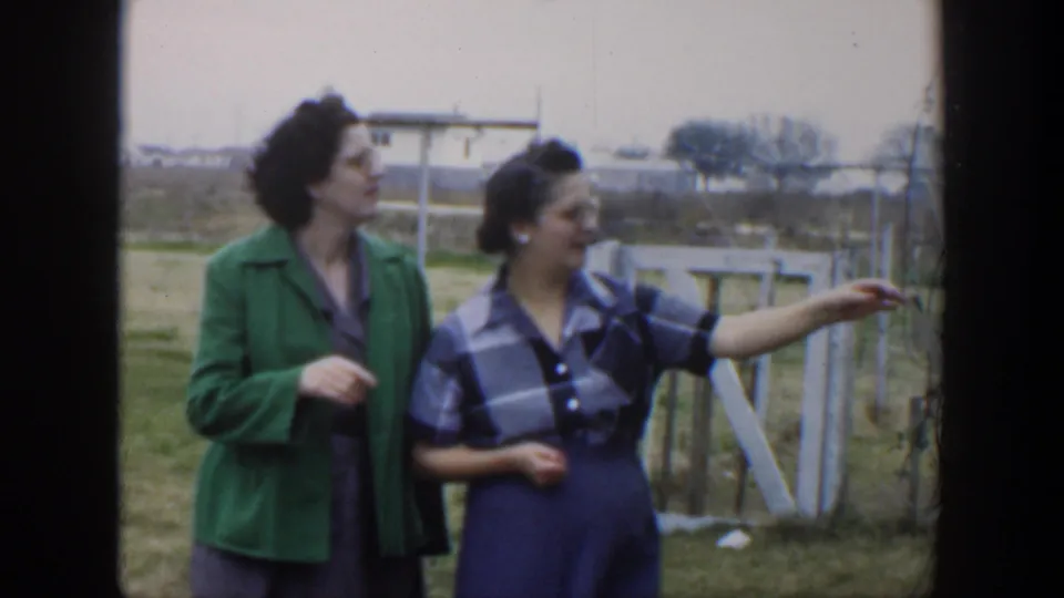 1951 Cuba frame of two women beside a white gate and wire fence, with one pointing across the grassy rural landscape.