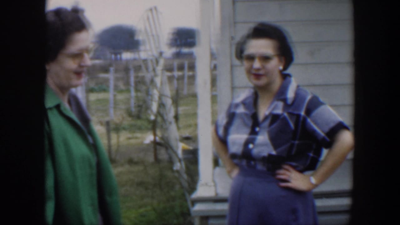 In metadata-identified 1951 Cuba, two adult women in glasses stand near house siding and porch posts during a casual outdoor conversation.