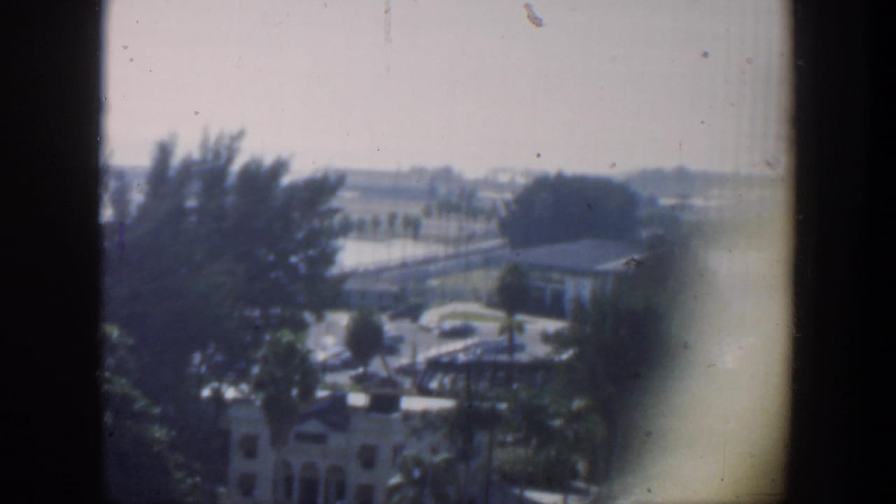 A soft 1951 Cuba 8mm frame shows an outdoor view with trees, vehicles, and dark film borders.