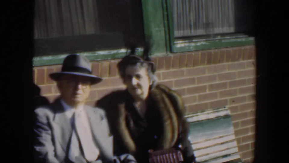 The 1951 Cuba home-movie frame shows the seated couple posing near green-trimmed windows, with the man partly cropped.
