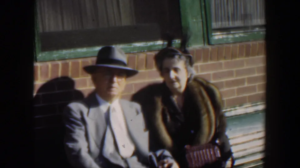 A 1951 Cuba frame centers the couple on the bench, with the man in a fedora and the woman holding a small handbag.
