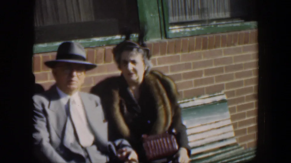 The final frame holds on the elderly couple in Cuba, seated close together with dressy 1950s clothing and a handbag visible.