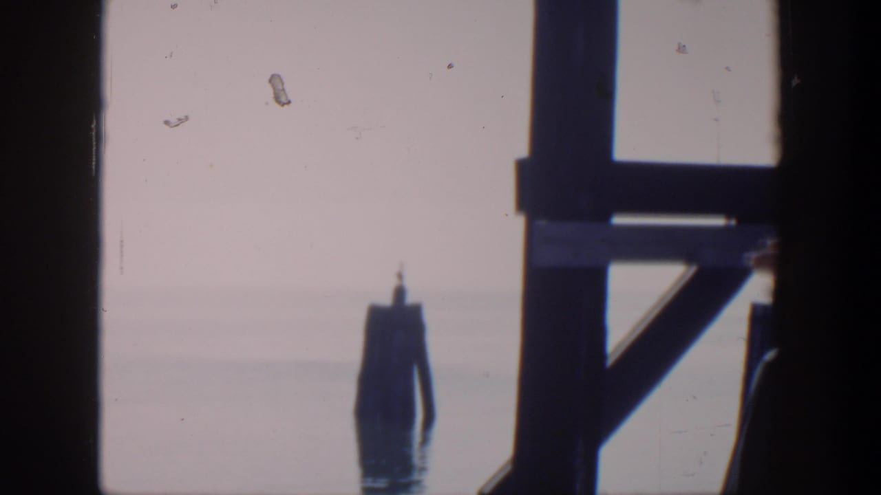 Pier structure frames a distant marker in calm water.
