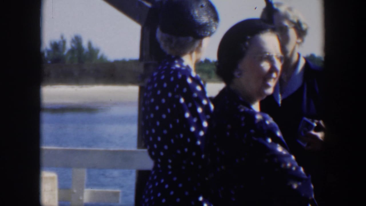 Three adults converse near a waterside railing, with one woman smiling toward the camera.