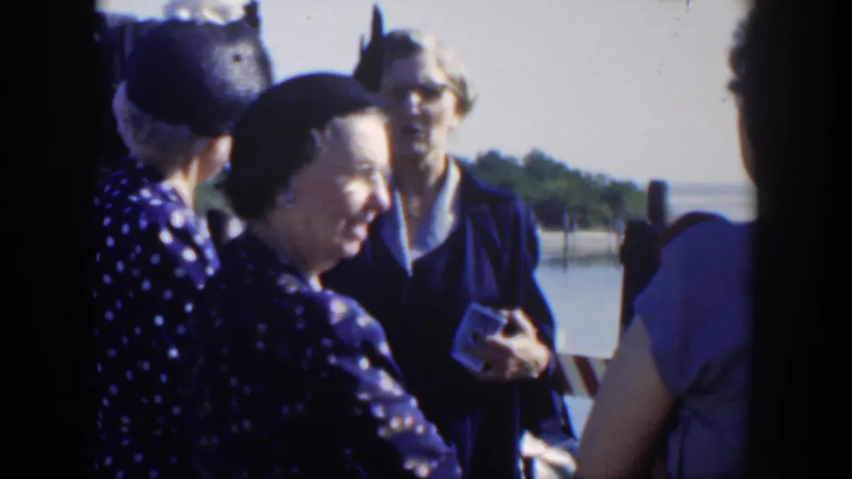 A close home-movie view shows women in mid-century dress smiling and talking beside the Cuban waterfront.