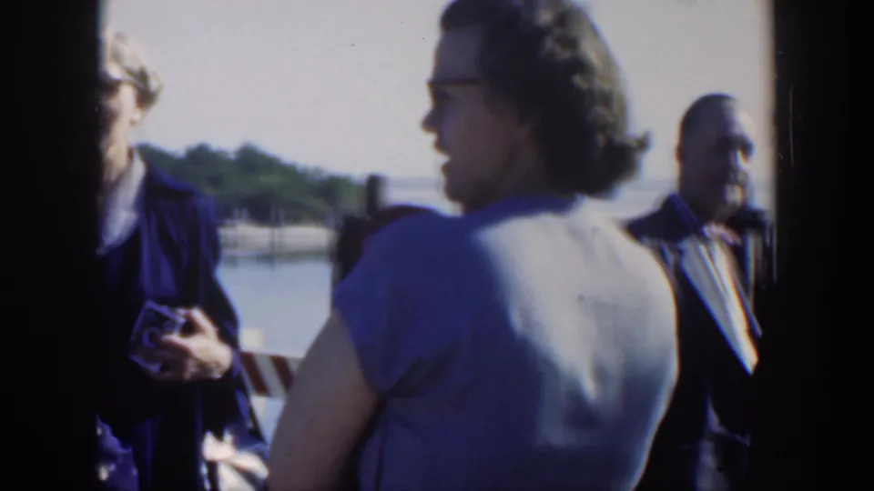 The 1951 Cuba clip shows a woman in a blue dress turned toward others beside a dockside waterfront.