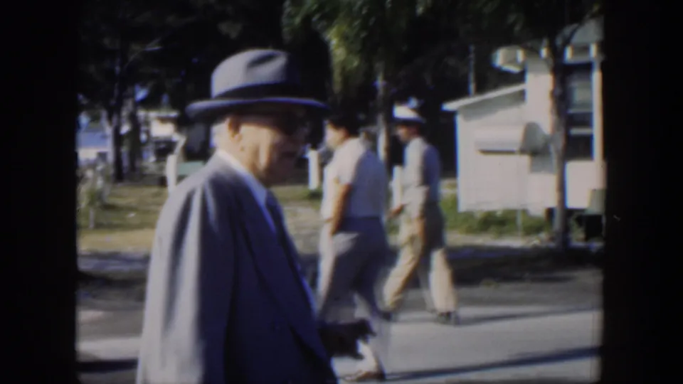 In the final frame, the suited man in a fedora is near other pedestrians and a small park structure in 1951 Cuba seaside footage.
