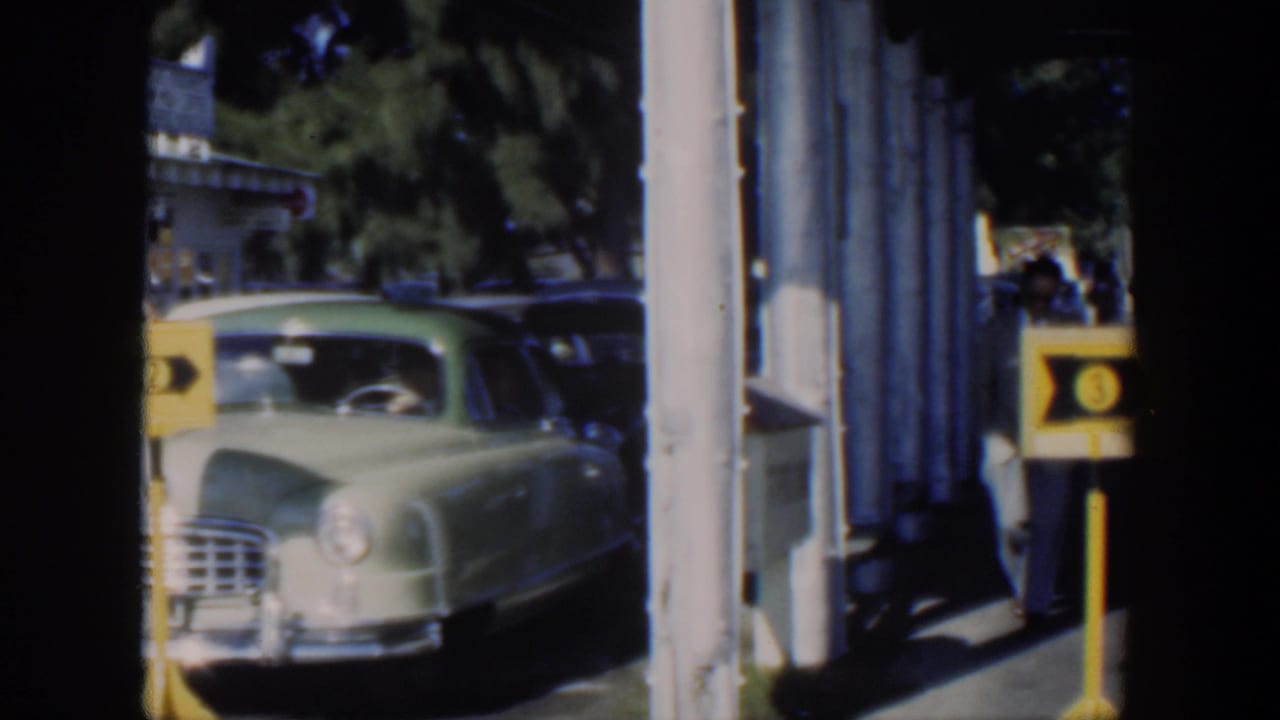 1951 Cuba 8mm frame showing a pale green American sedan near columns and a yellow service sign in bright daylight.
