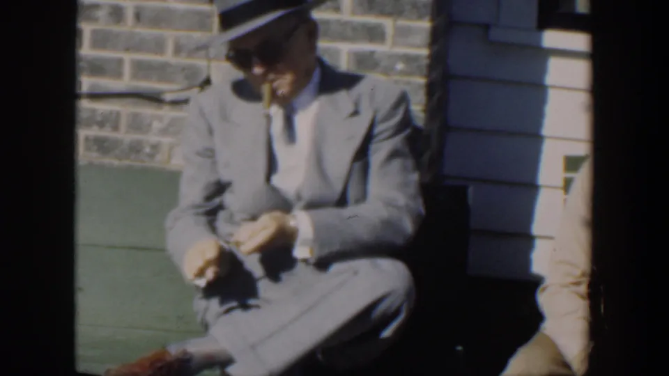 The 1951 Cuba home-movie frame shows the suited man on a green bench, apparently sharpening or handling a pencil with a small tool.