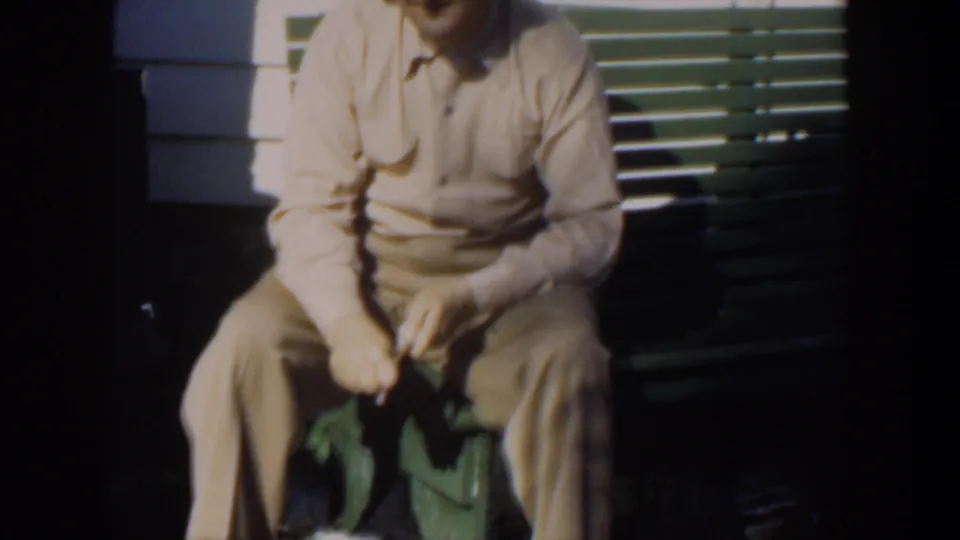 The seated man remains on the porch bench, partly cropped, with his hands gathered around a small object in bright light.