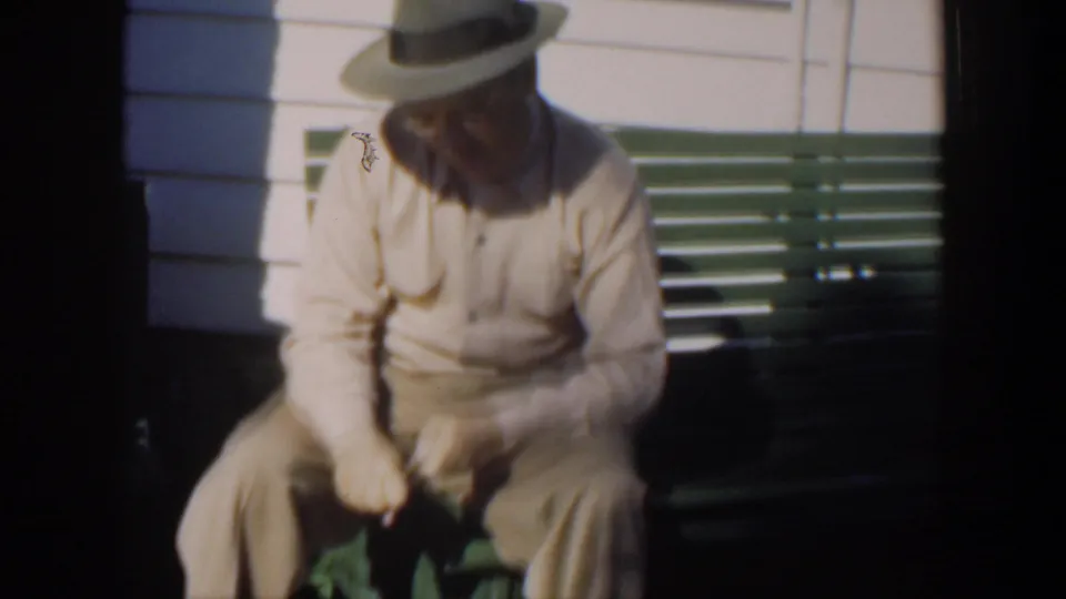 The 1951 Cuba footage shows the older man bent slightly forward on the bench, focused on the small item in his hands.