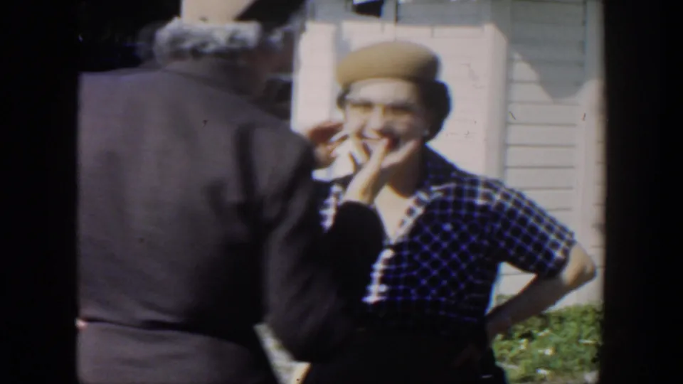 1951 Cuba frame showing a woman in a plaid shirt and beret laughing as an older woman stands close by outside the house.