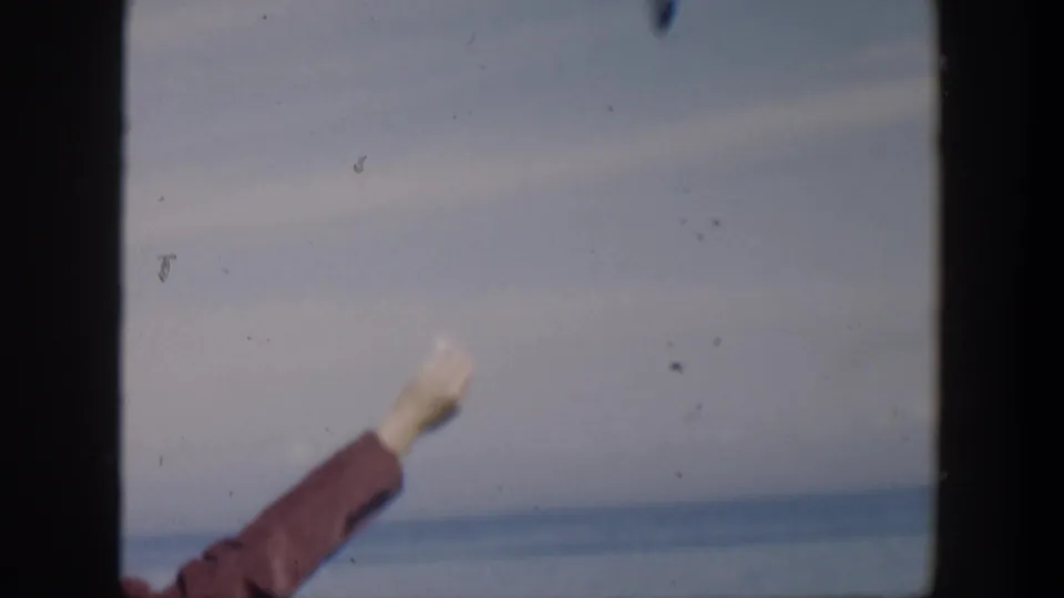 A red-sleeved arm extends into a soft 8mm view of ocean and sky, continuing the gesture seen in the Cuba 1951 clip.