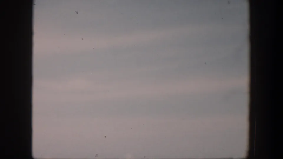 1951 Cuba 8mm frame of a muted coastal sky with thin cloud bands, light grain, dust specks, and dark scan borders.