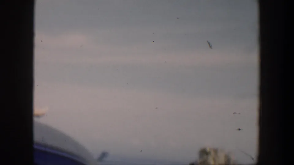 Soft 8mm frame from Cuba in 1951 showing a partial figure, car edge, cloudy sky, and ocean horizon.
