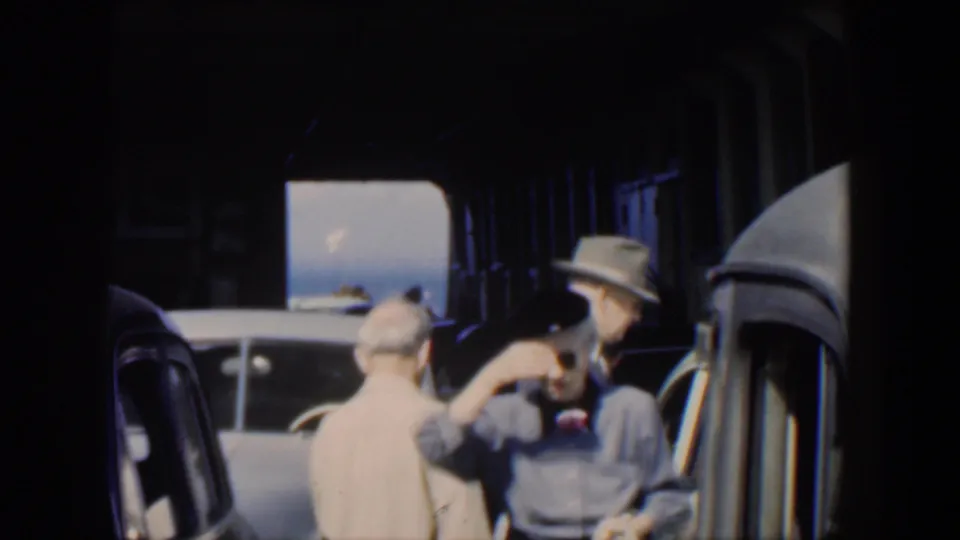 1951 Cuba transport scene with adults around classic cars and a woman lifting her hand near her sunglasses.