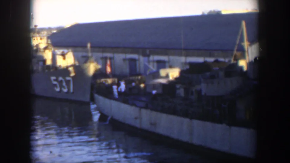 1951 Cuba home-movie frame of a harbor with vessel 537, a docked boat, pier details, and a large waterfront building behind.