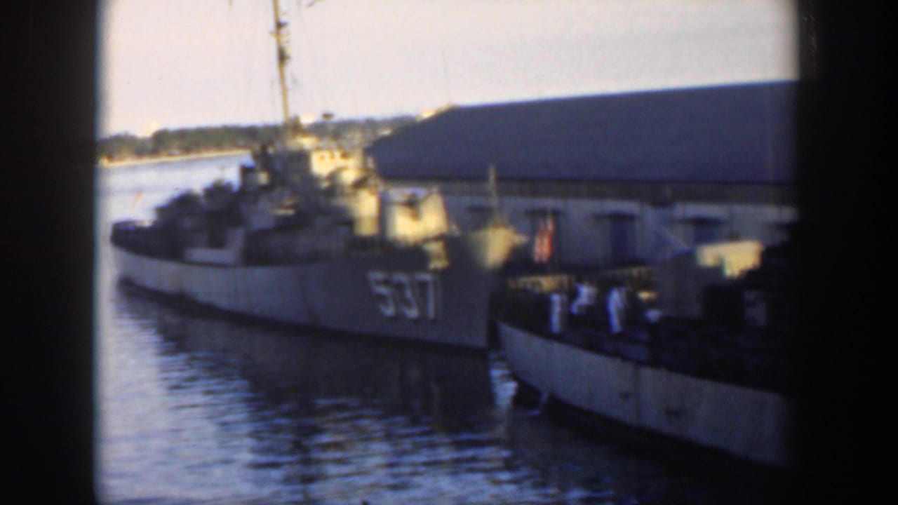 1951 Cuba home-movie frame showing a gray U.S. Navy destroyer marked 537 moored beside a pier, with crew figures on deck and harbor water below.